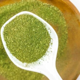 Coarse grind Mitragynina speciosa or Kratom powder in white ceramic spoon on wooden bowl