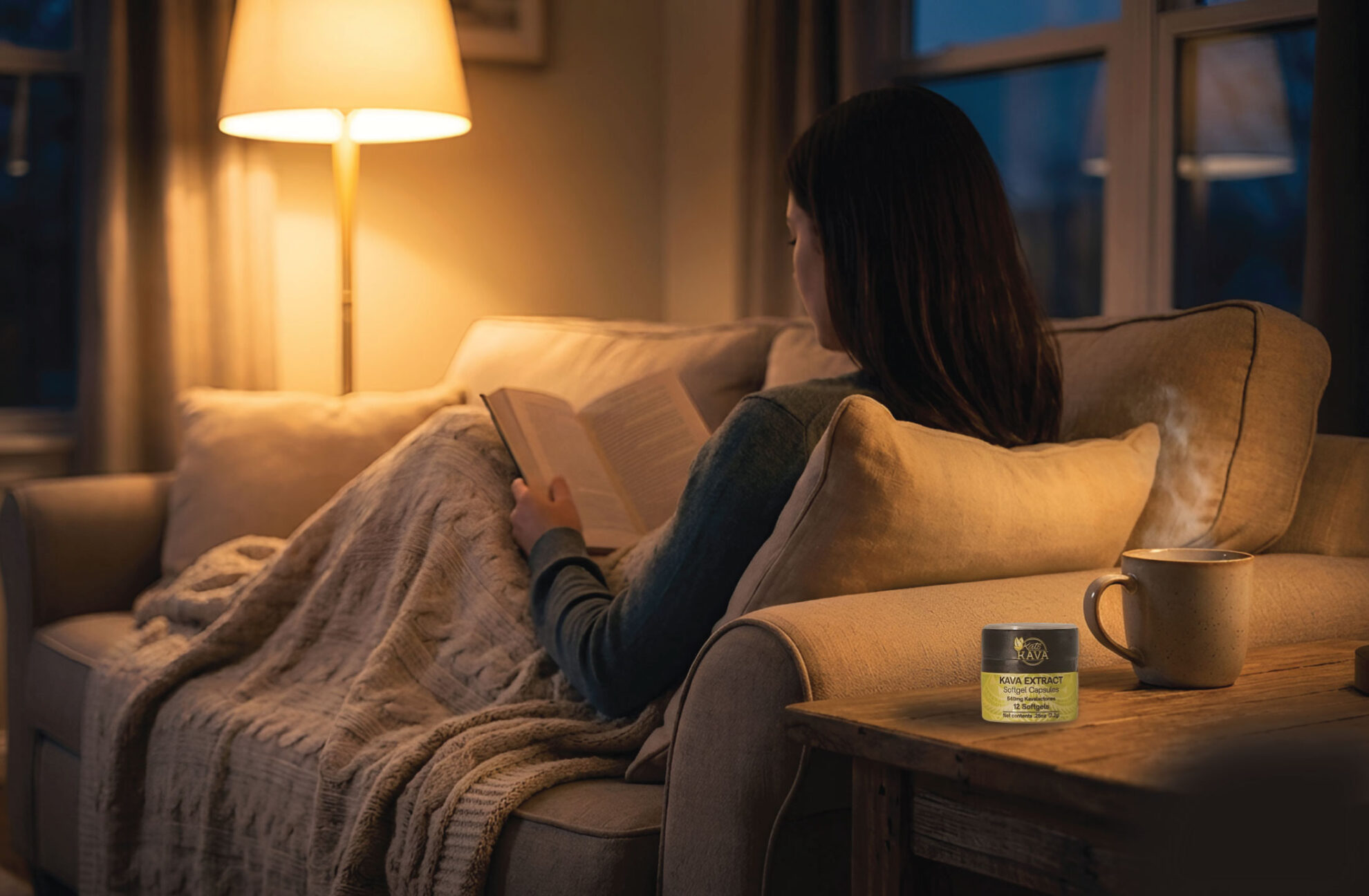 A person sits on a cozy couch under a blanket, reading a book by lamplight. A jar of skincare cream and a mug are on the wooden side table nearby.