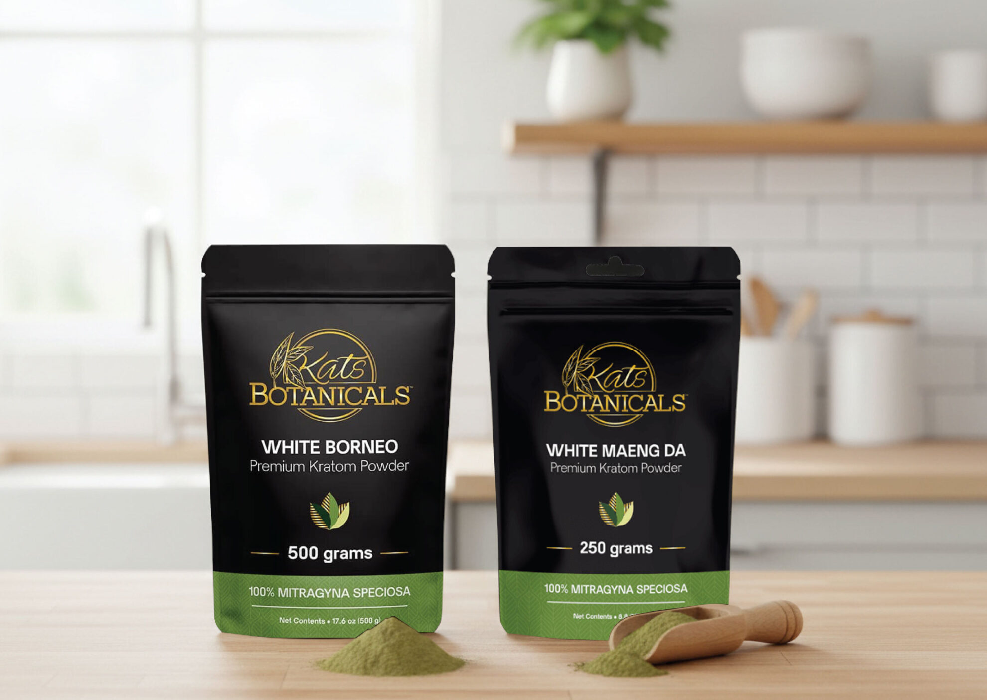 Two black pouches of Kat’s Botanicals kratom powder, labeled White Borneo (500 grams) and White Maeng Da (250 grams), stand on a kitchen counter with small piles of green powder and a wooden scoop in front.
