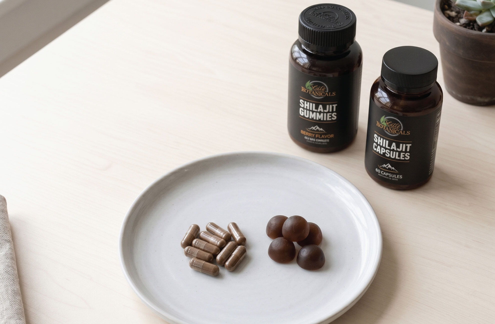 Two bottles labeled Shilajit Gummies and Shilajit Capsules sit on a light table next to a plate with several brown gummies and capsules. A potted succulent is in the corner.