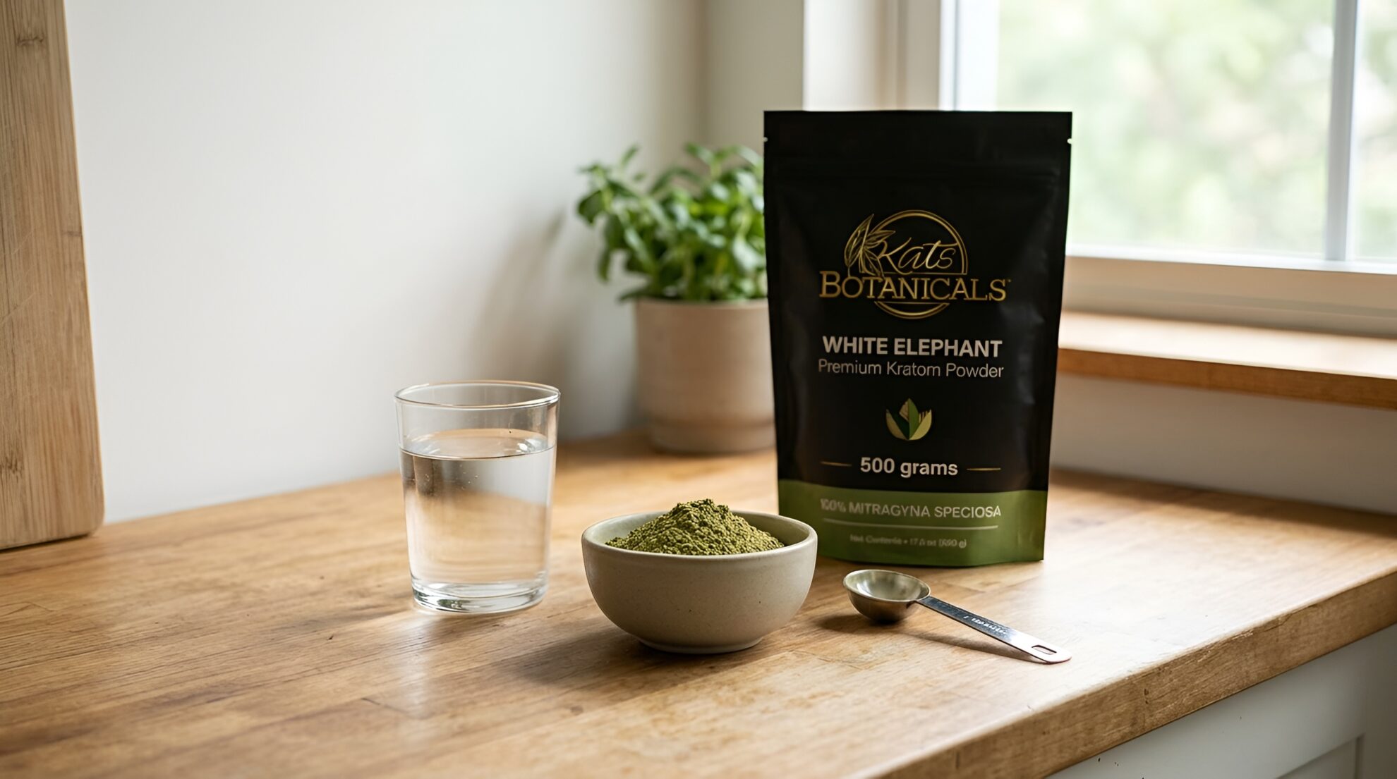 A bag of Kats Botanicals White Elephant kratom powder next to a small bowl of the powder, a measuring spoon, and a glass of water on a wooden counter.