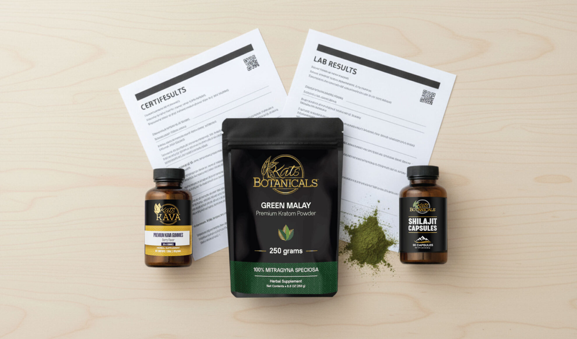 A packet of Green Malay kratom powder and two supplement bottles are displayed on a wooden surface, with product information sheets and a small pile of green powder beside the packet.