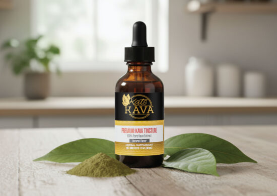 A brown glass dropper bottle labeled Kats Kava Premium Kava Tincture stands on a wooden surface, surrounded by kava leaves and a small pile of kava powder, with a blurred background.