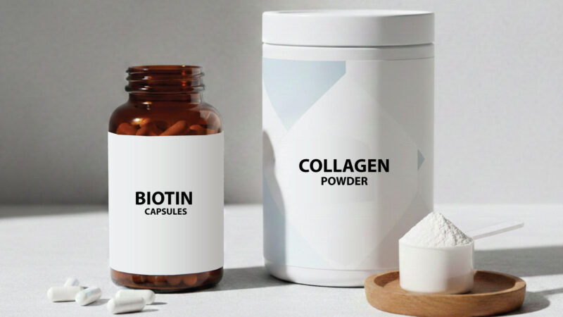 A brown bottle labeled Biotin Capsules is next to a white container labeled Collagen Powder with a small wooden tray holding a scoop of white powder and some capsules on a light surface.
