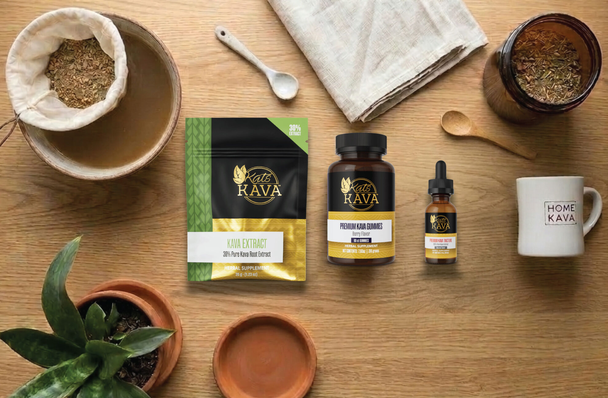 A wooden table with kava tea-making items, a plant, a cup labeled HOME KAVA, a pouch of Kava Rava Kava Extract, a bottle of Kava Rava Premium Kava Extract, and a dropper bottle of Kava Rava tincture.