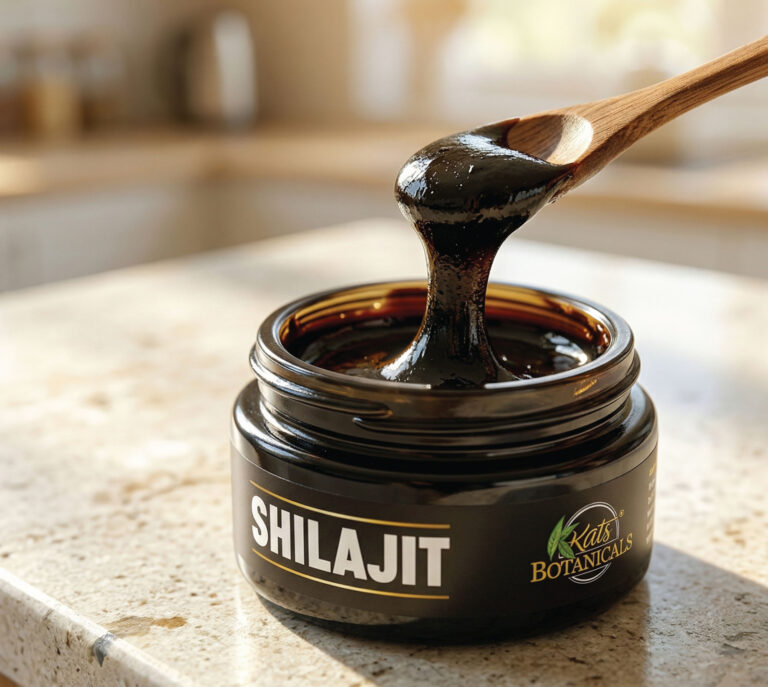 A wooden spoon lifts thick, dark shilajit resin from an open jar labeled SHILAJIT by Kats Botanicals, resting on a sunlit kitchen counter.