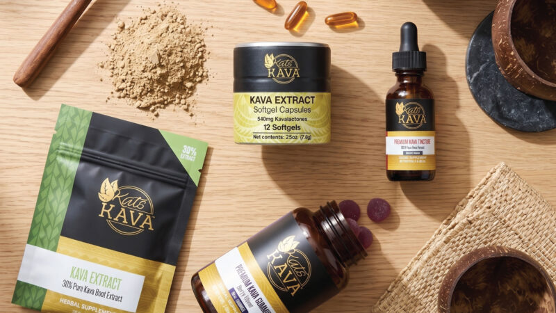 A selection of Kat’s Kava products, including capsules, powder, tincture, extract, and gummies, arranged on a wooden surface with bowls and a wooden spoon.