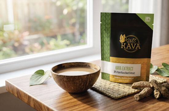A wooden bowl filled with a light brown liquid sits next to a Kats Kava extract package on a wooden table, with sunlight streaming through a nearby window.