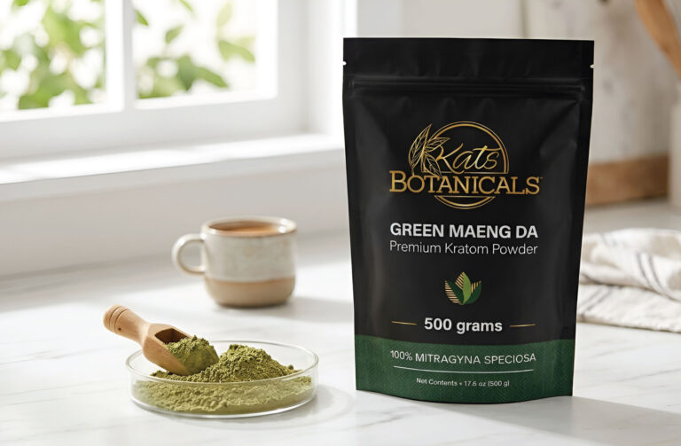 A bag of Kats Botanicals Green Maeng Da Kratom powder sits on a kitchen counter next to a mug, a cloth, and a small plate with powder and a wooden scoop.